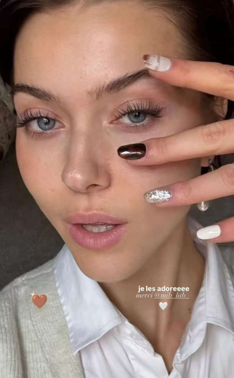 Portrait rapproché : la modèle montre ses press-on nails blancs, brun chocolat et argent pailleté, avec le texte “merci @mib_lab_”.