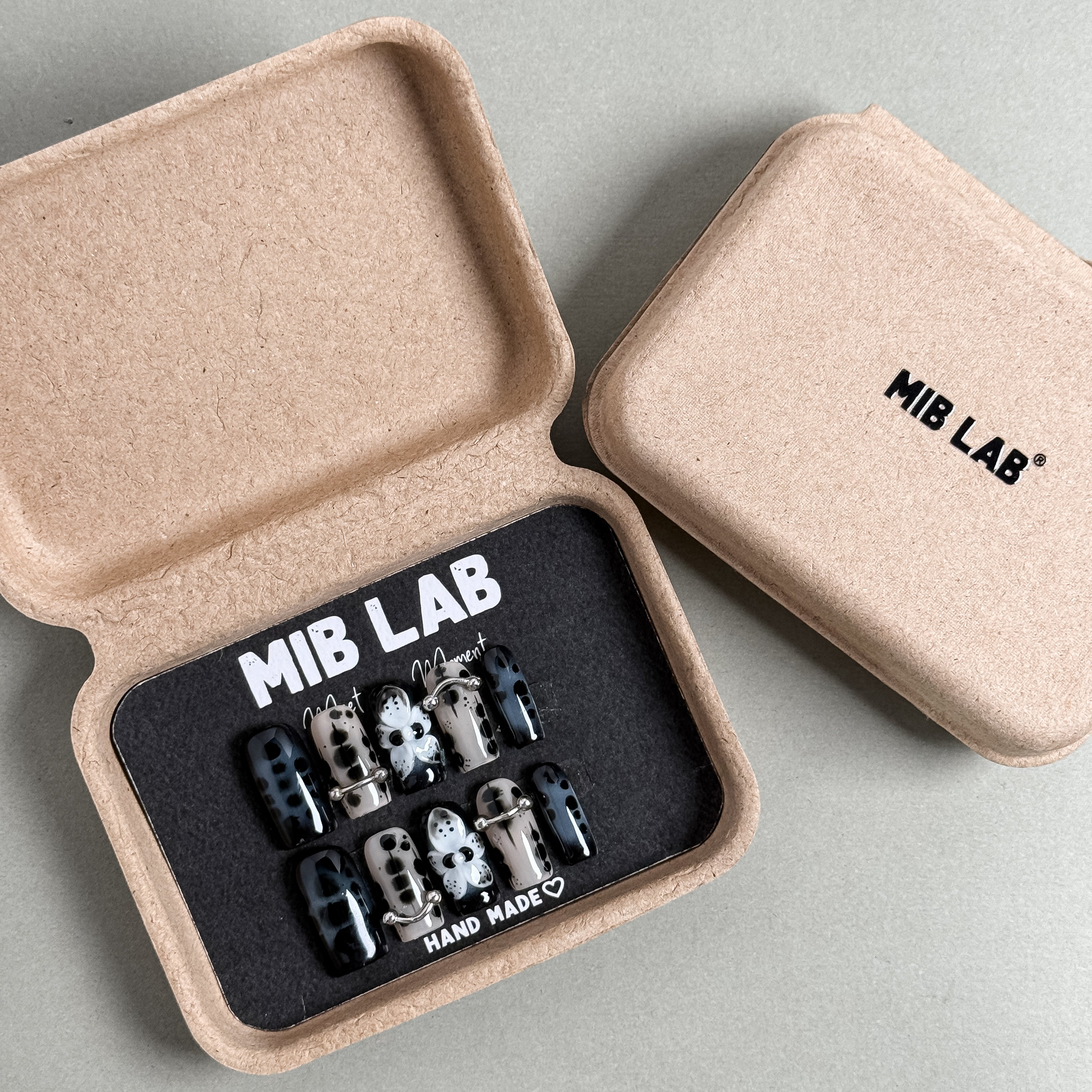 MIBLAB Bones press-on nail set featuring spooky skeleton patterns in metallic black and silver tones, packaged for boutique display in Geneva.