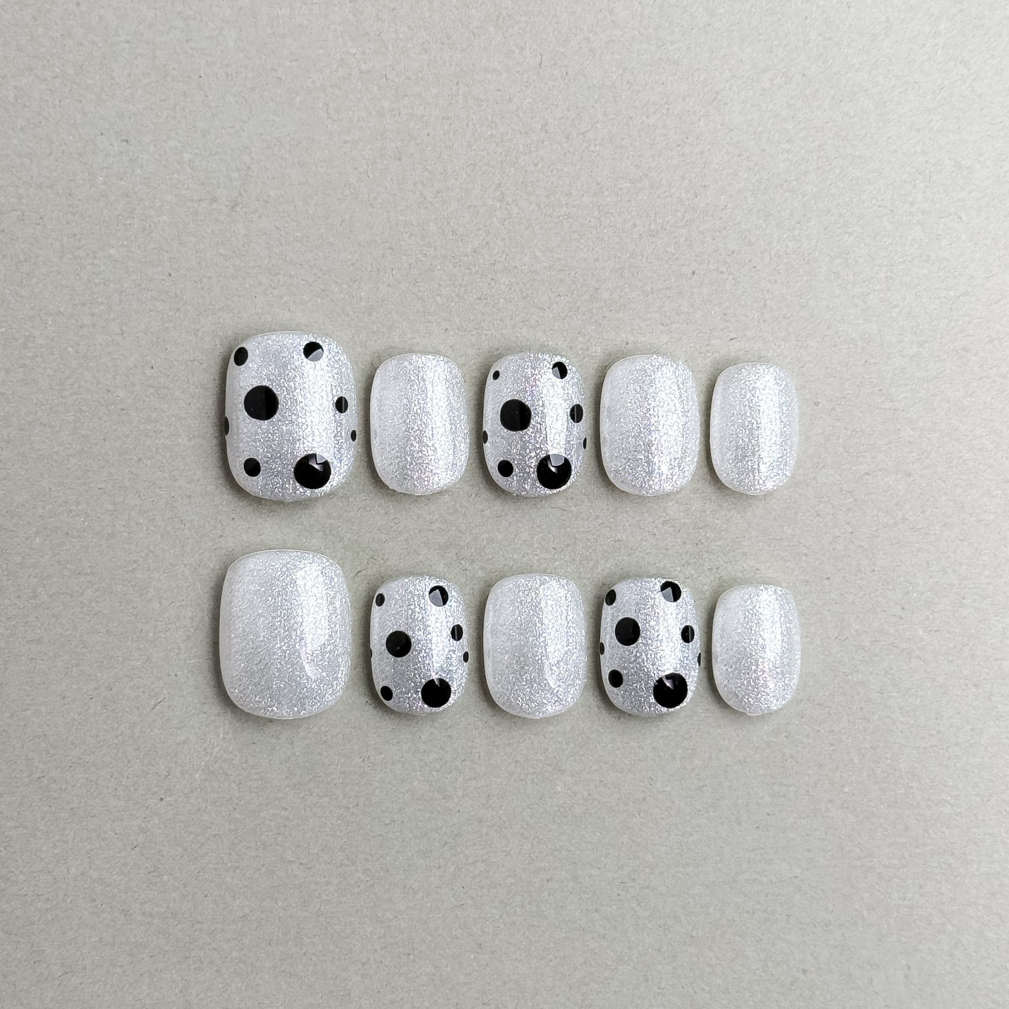 Just : faux ongles réutilisables blanc laiteux avec pois noirs, press on nails premium, finition brillante style minimal.