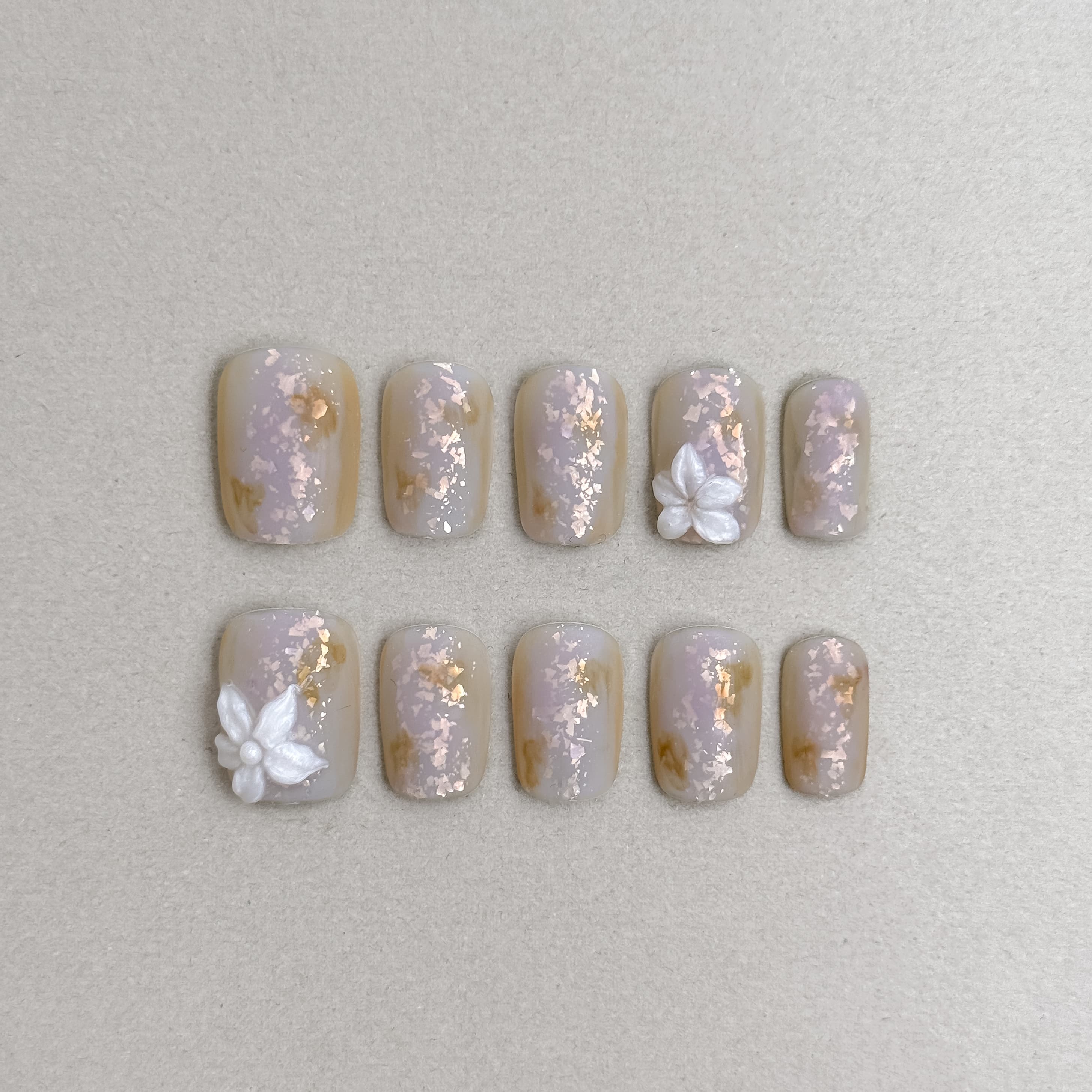 Le Toi : faux ongles réutilisables nude beige nacré, motifs floraux blancs et accents dorés, press on nails premium, finition brillante.
